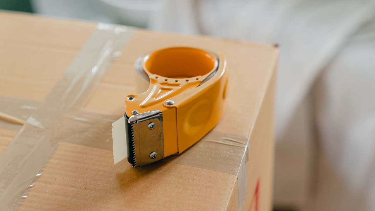 A yellow tape dispenser resting on a sealed cardboard shipping box