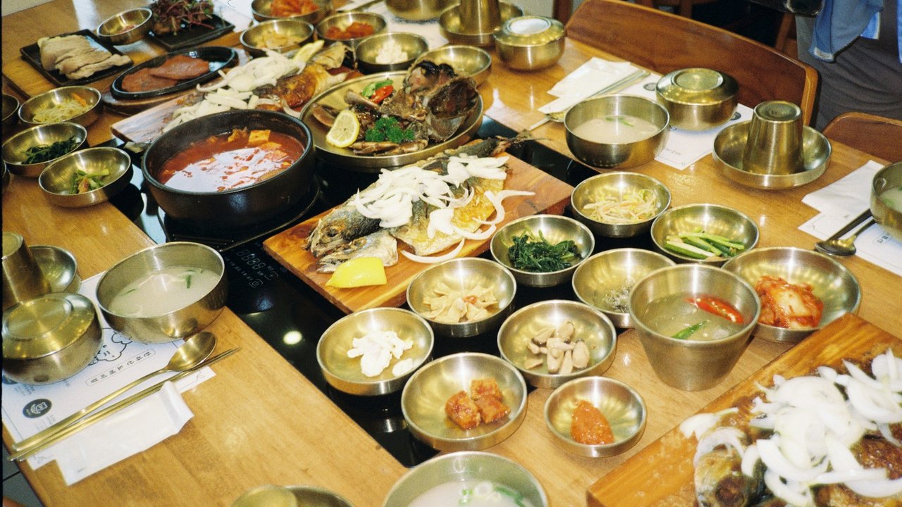 A wooden table filled with Korean dishes, stews and many small side dishes in brass bowls